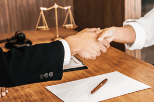 Attorney and client shaking hands during a legal consultation, symbolizing support and representation.